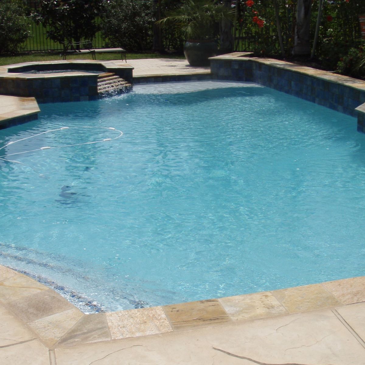 Backyard swimming pool with blue water and beige stone patio surrounding it