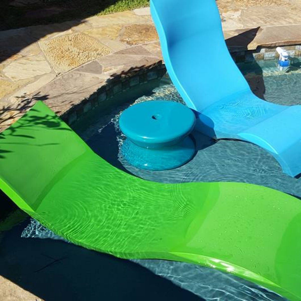 Two bright inflatable pool loungers, one green and one blue, floating in a backyard pool