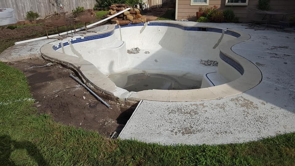 Empty in-ground swimming pool under construction, with white concrete and surrounding patio area.