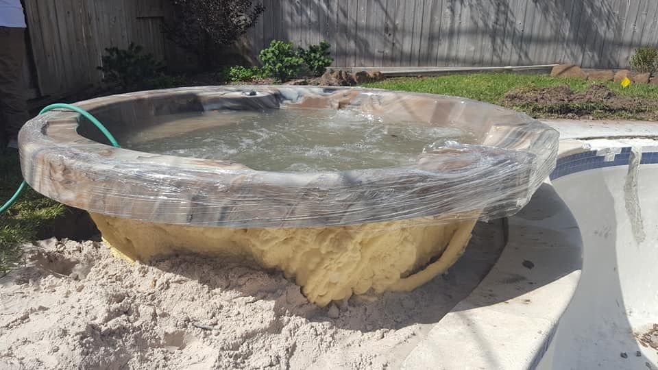 Shallow stone birdbath in a sunny garden, with water and a green hose nearby