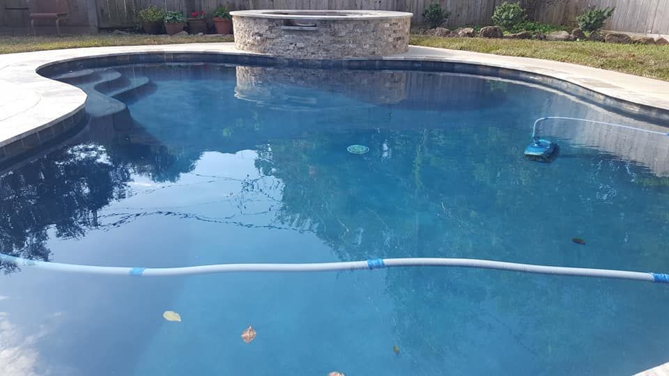 Backyard swimming pool with a stone waterfall, blue water, and a cleaning hose floating across the surface