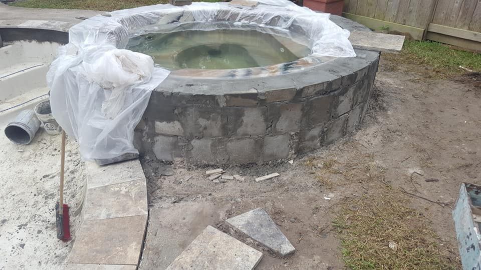 Partially built round stone hot tub with plastic covering, surrounded by dirt and construction debris