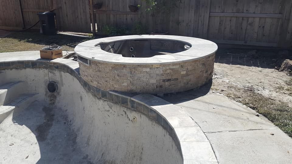 Empty backyard pool with a raised circular stone spa and curved concrete deck under construction