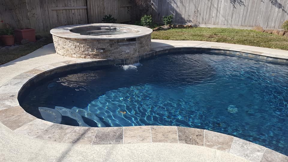 Backyard swimming pool with a raised stone spa and blue water beside a wooden fence