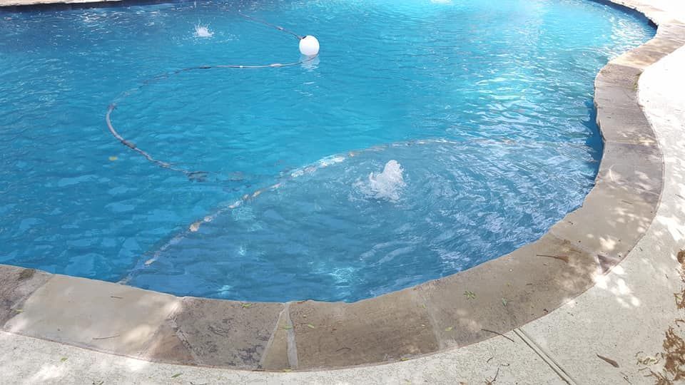 Curved blue swimming pool with a wet stone edge and a floating white ball