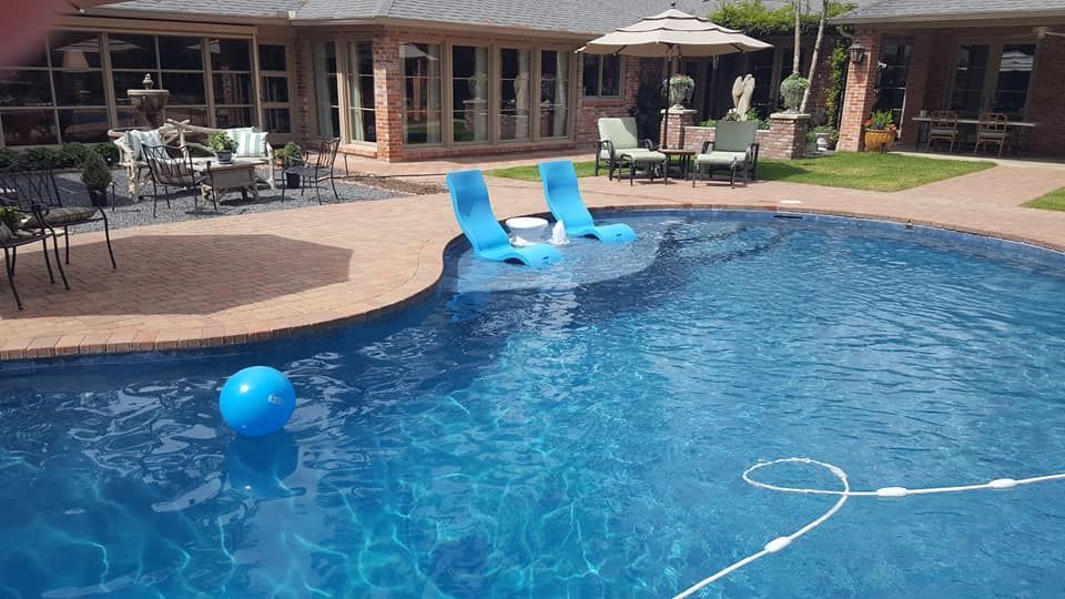 Backyard pool with two blue lounge chairs, a blue float ball, and a white pool noodle in the water