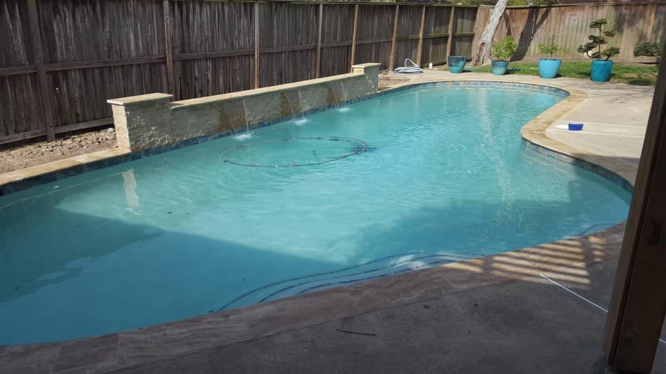 Backyard swimming pool with clear blue water, surrounded by a wooden fence and stone deck area