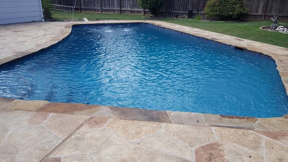 Backyard swimming pool with blue water and stone patio surround