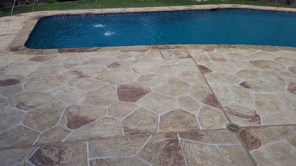 Stone patio beside a blue swimming pool with grass at the edge