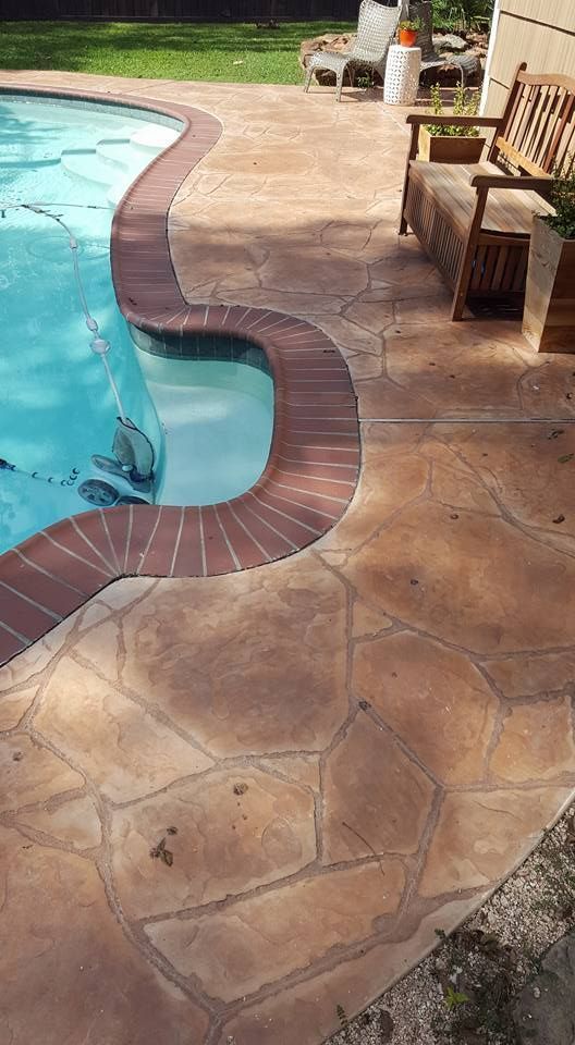 Curved backyard pool edge with tan stone patio and blue water in sunlight