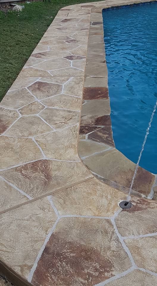 Stone pool deck beside blue swimming pool with curved edge and drain fixture