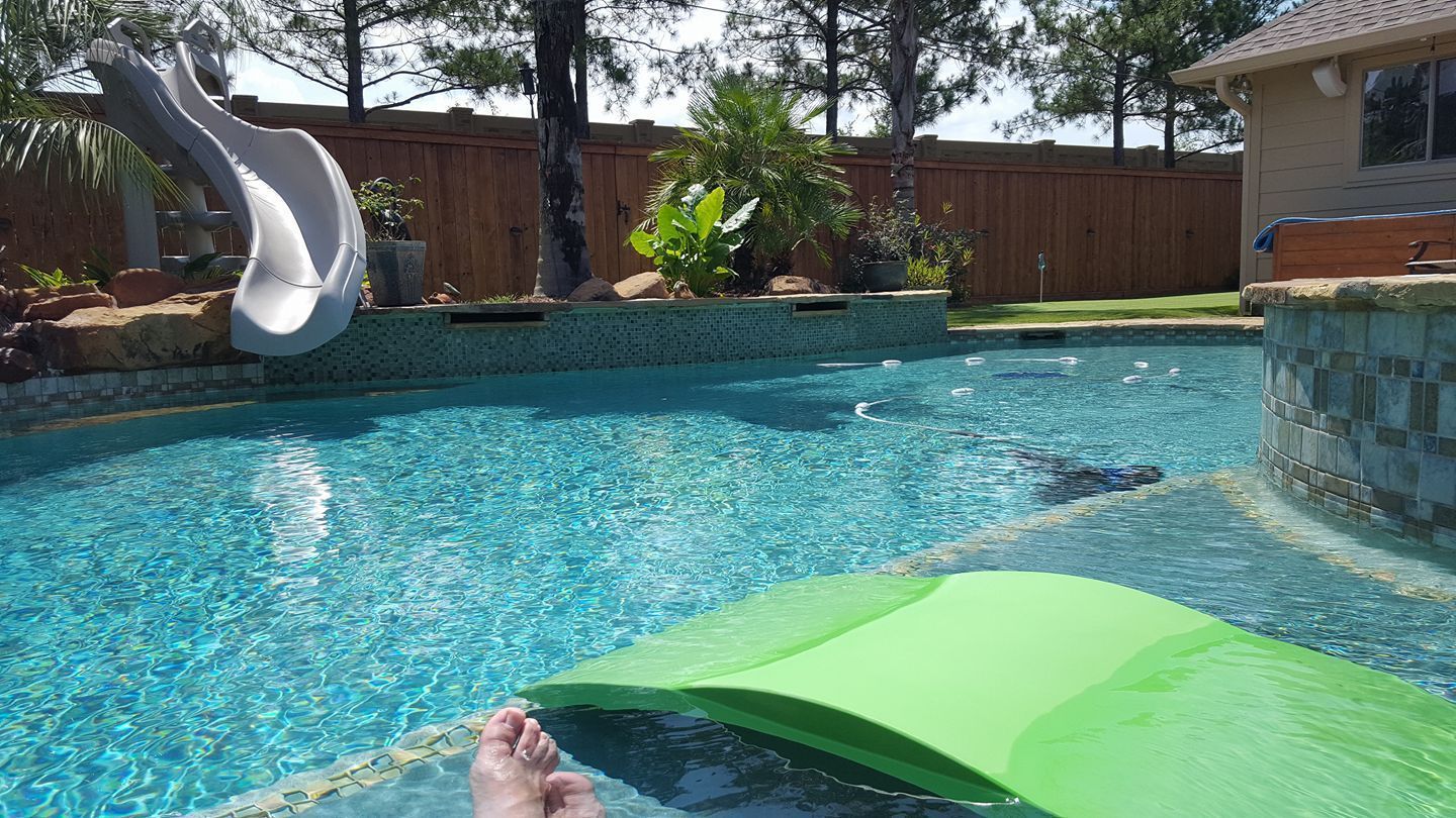 Backyard pool with a waterslide, floating green lounger, and sunlit blue water