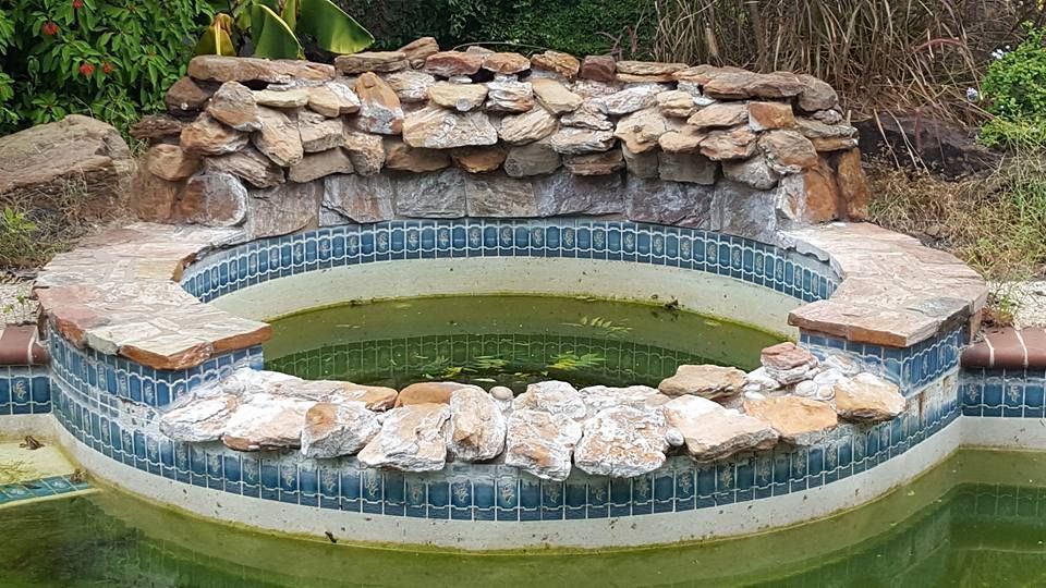 Small round stone-lined pond or hot tub with blue tile border and stacked rocks in a garden setting
