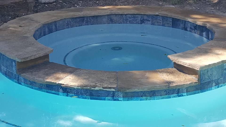 Round blue hot tub built into a stone pool deck with clear water.