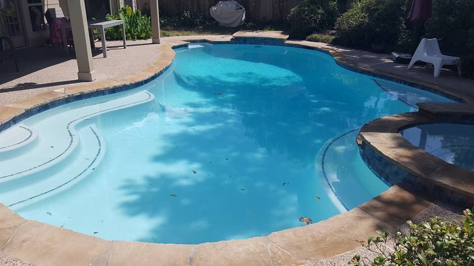 Curved backyard swimming pool with blue water, tan deck, and lounge chairs in the sun