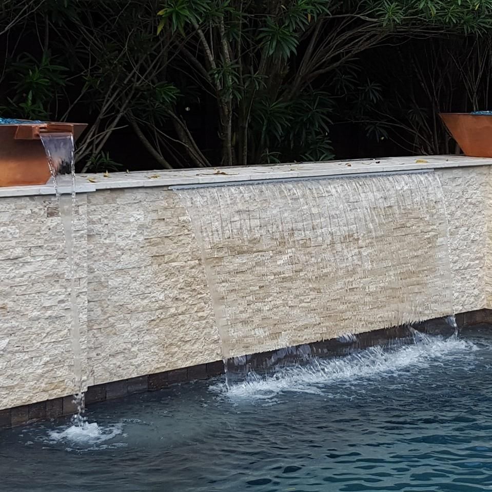Stone fountain wall with water spilling into a blue pool, framed by dark green plants