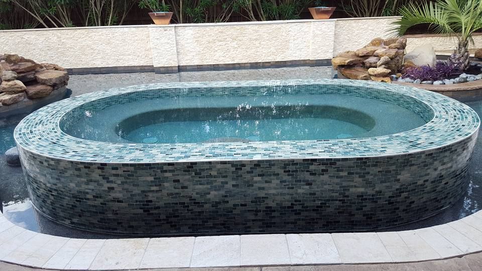Round tiled hot tub in a backyard patio, filled with water and surrounded by rocks and potted plants.