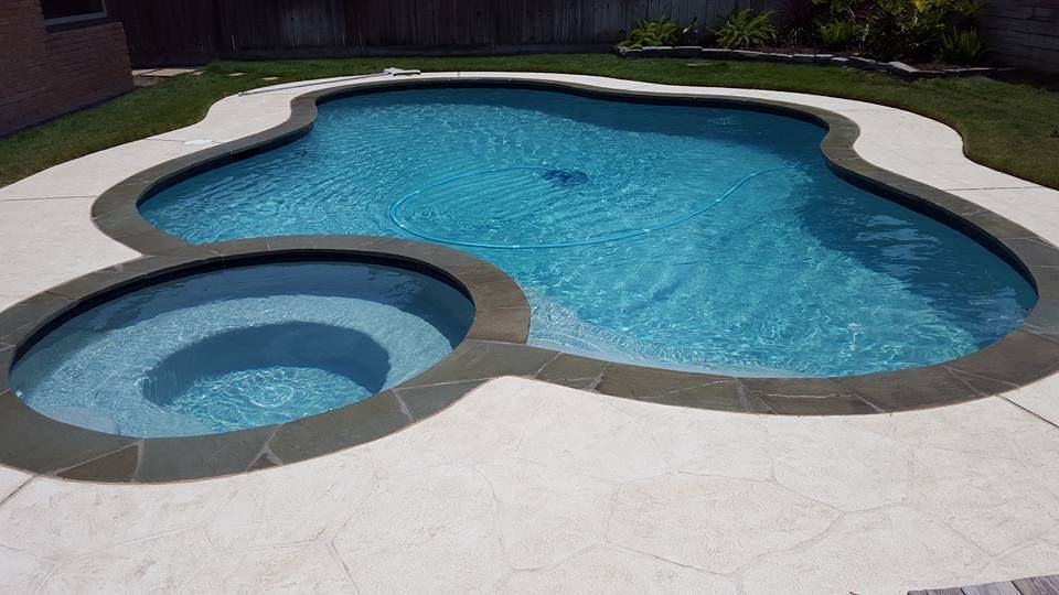 Backyard swimming pool with attached hot tub and light stone patio under bright sun