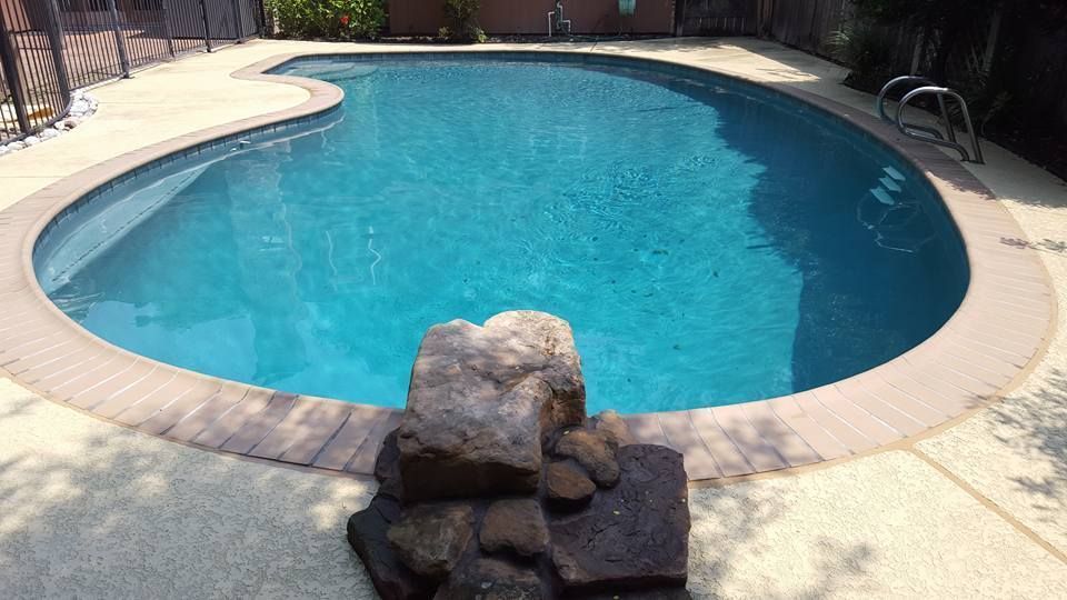 Curved backyard swimming pool with blue water and a stone waterfall feature in the foreground
