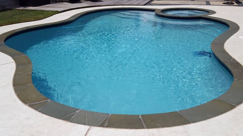 Backyard swimming pool with blue water, curved shape, and a built-in spa area