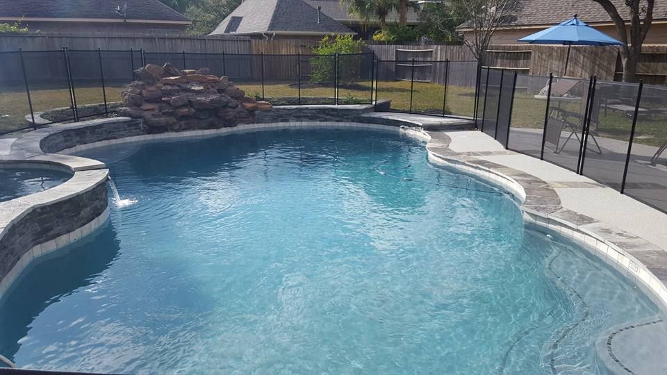 Backyard swimming pool with blue water, stone coping, and patio fencing in bright sunlight