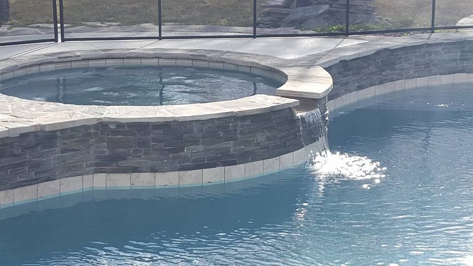 Backyard pool with a raised hot tub spilling water into the blue pool