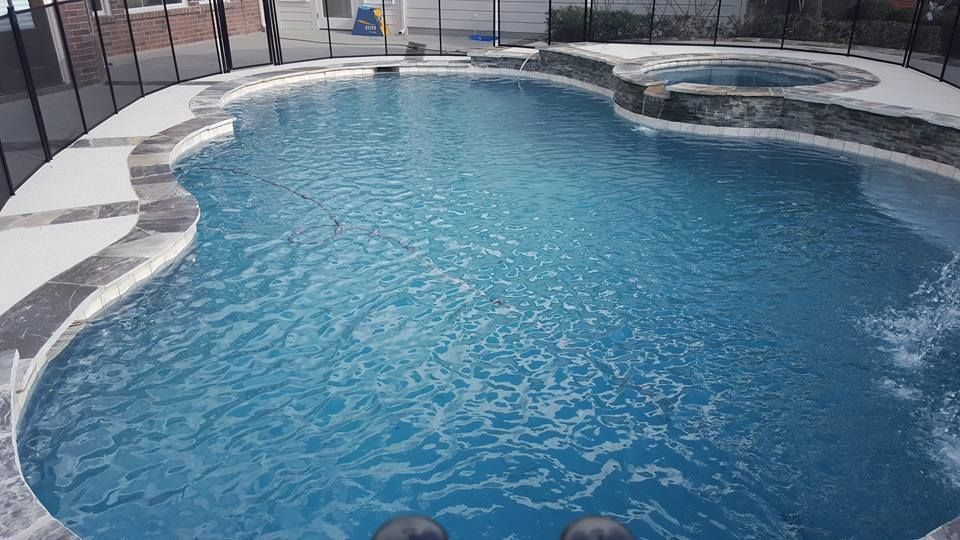 Curved backyard swimming pool with blue water and light stone coping