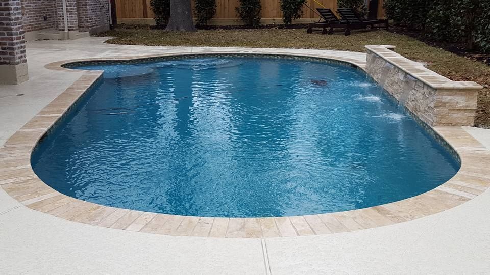 Curved blue swimming pool with beige stone deck in an outdoor courtyard
