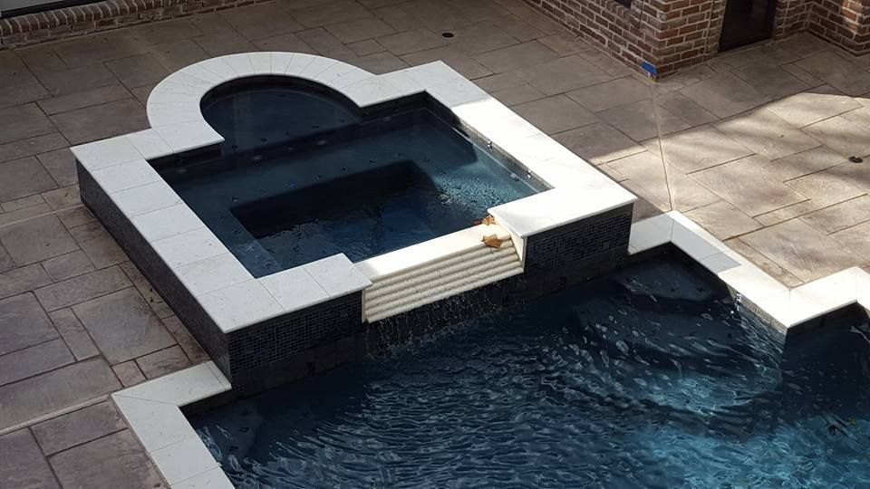 Small white-and-black tiered water feature with dark blue water beside a tiled patio