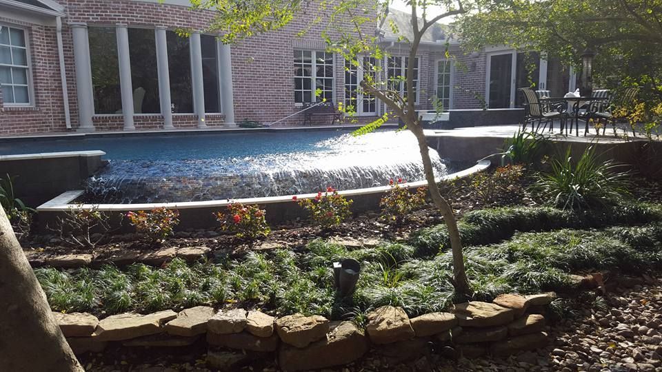 Courtyard fountain surrounded by landscaped garden beds and stone edging in front of a brick building