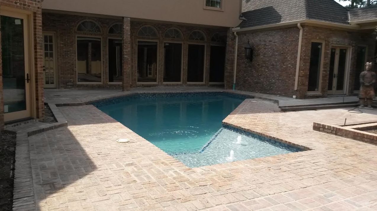 Backyard patio with a swimming pool beside a brick house and stone deck