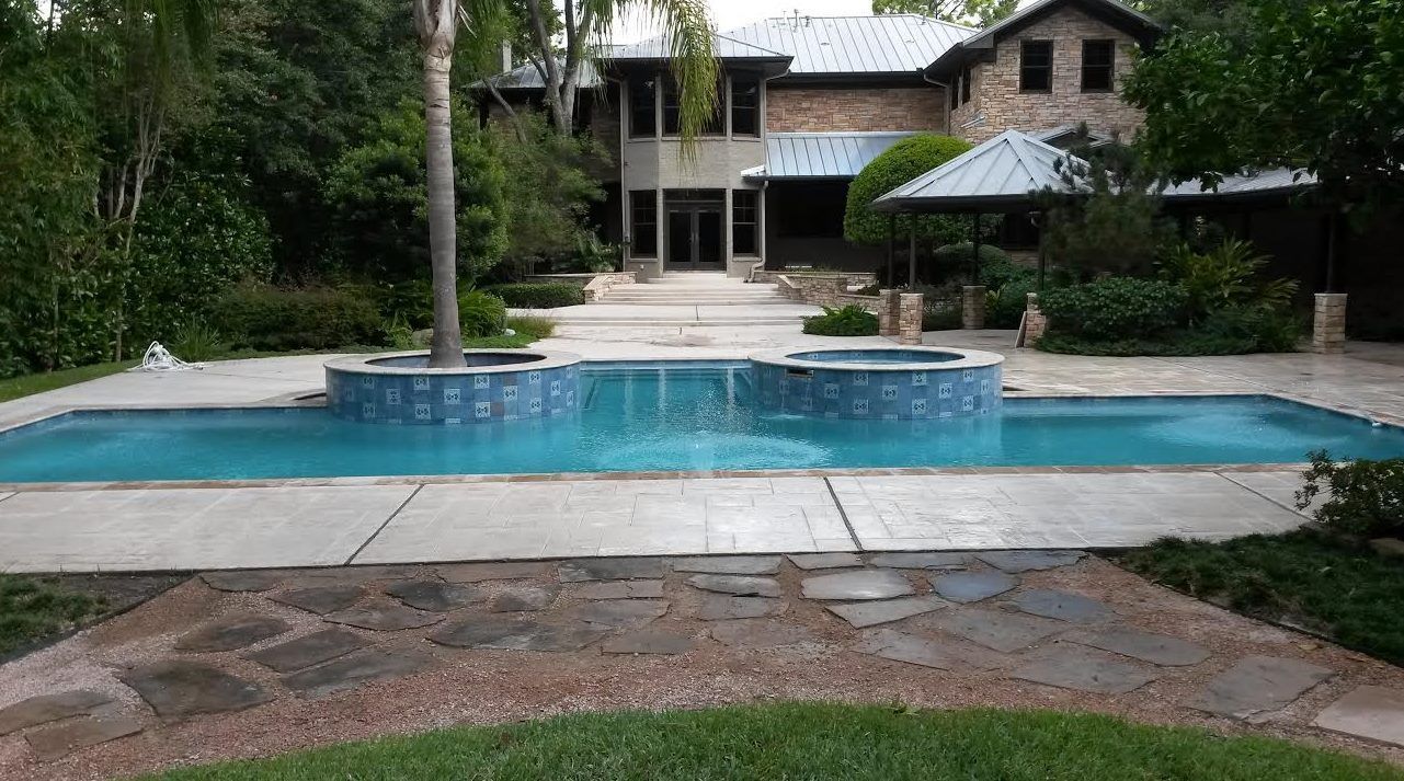 Backyard swimming pool with stone patio and a house surrounded by greenery