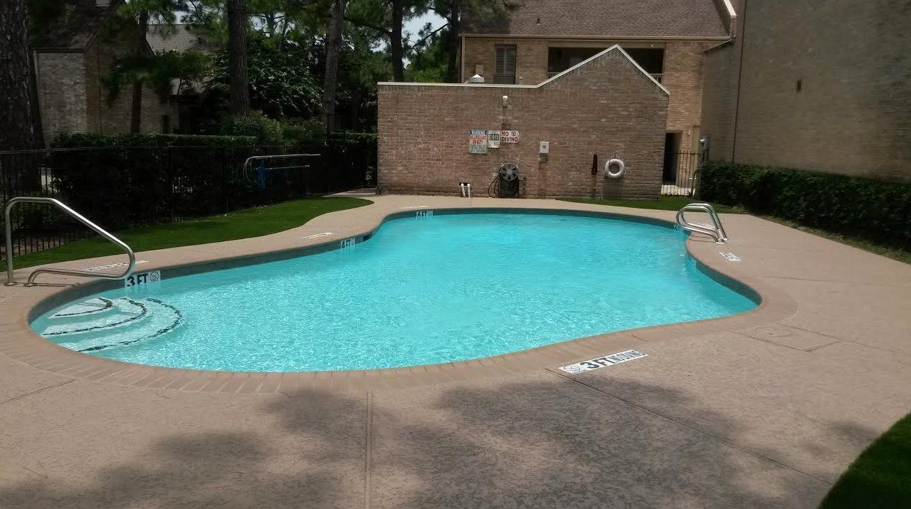 Backyard swimming pool with turquoise water, surrounded by beige concrete and a brick wall in the background
