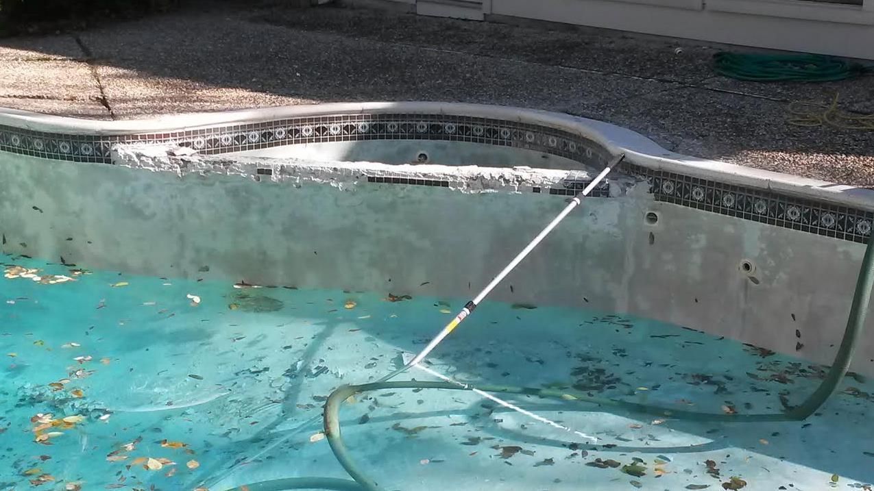 Swimming pool with turquoise water, a pool vacuum hose, and debris floating near the edge.