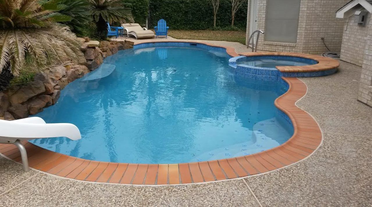 Backyard swimming pool with blue water, terracotta border, and a spa beside a patio.