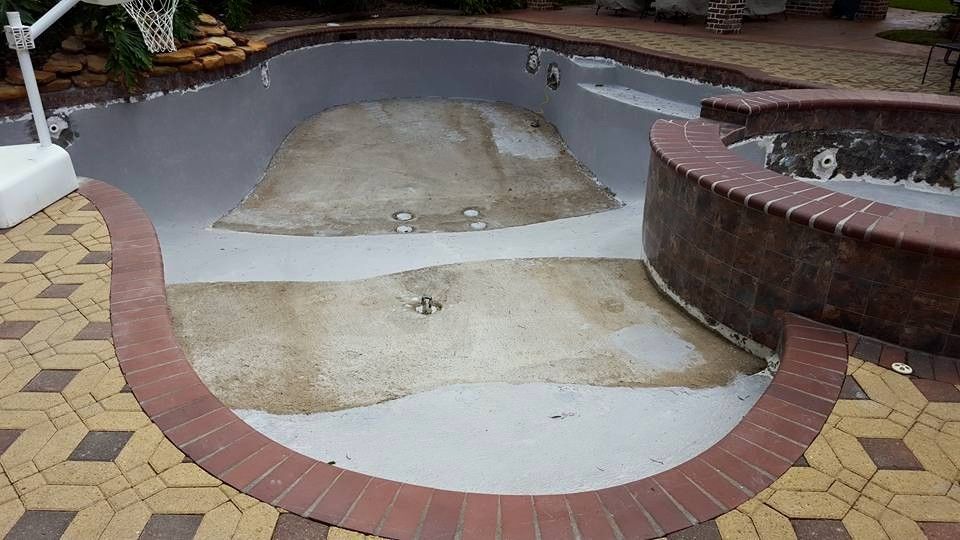 Empty drained swimming pool with cracked concrete and brick coping, viewed from above.
