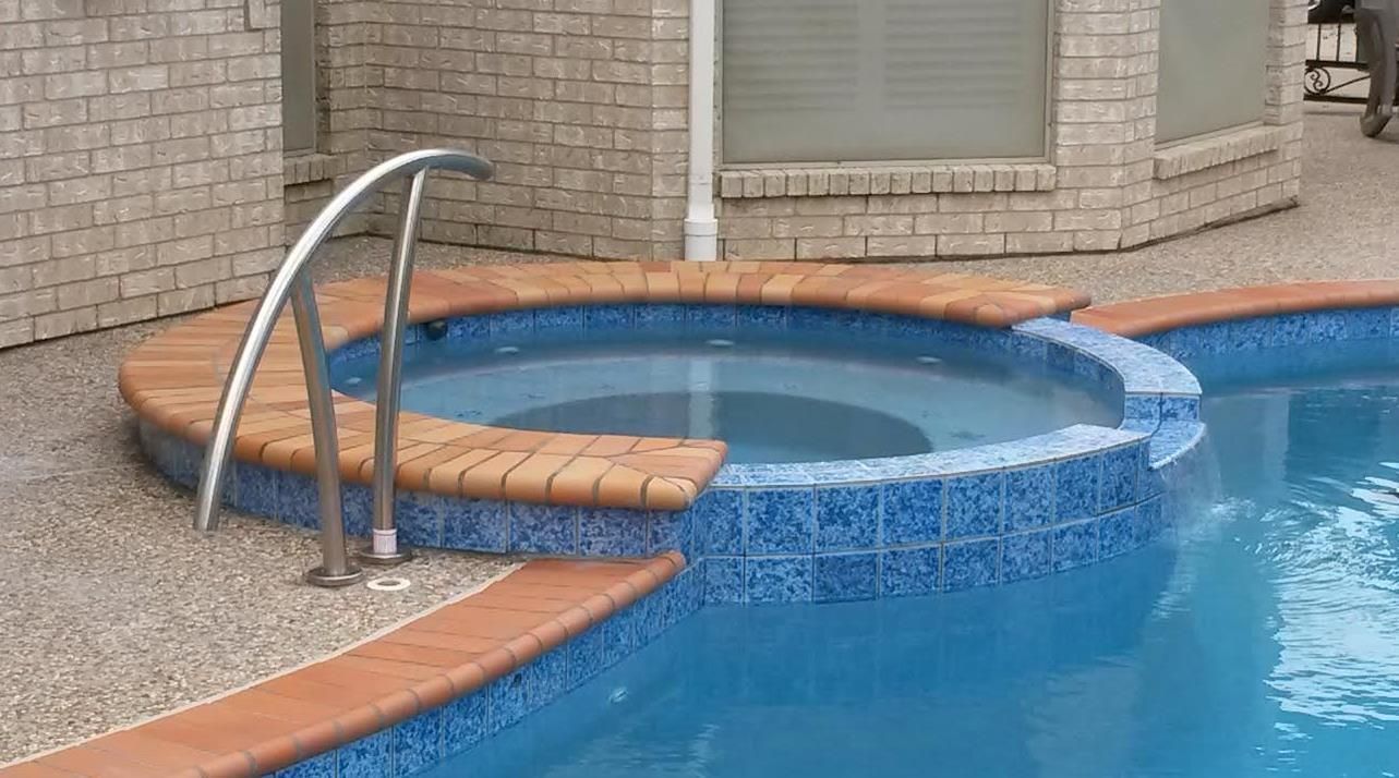 Curved pool steps with metal handrail beside a blue tiled swimming pool and brick patio