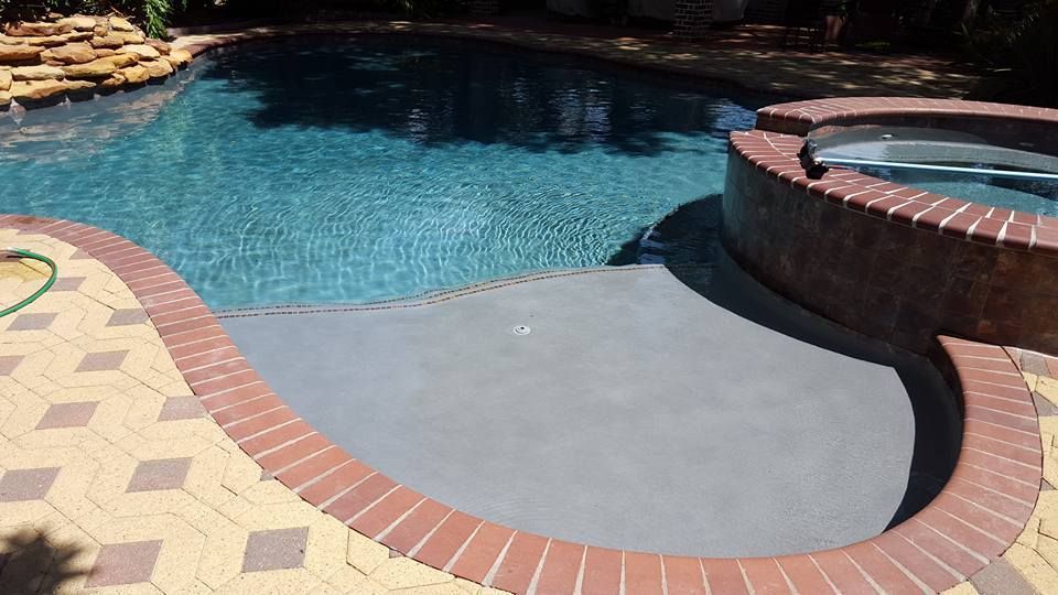 Backyard pool with blue water, curved brick coping, and a raised hot tub edge
