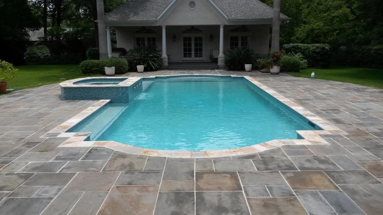 Backyard swimming pool with turquoise water and gray stone patio in front of a house