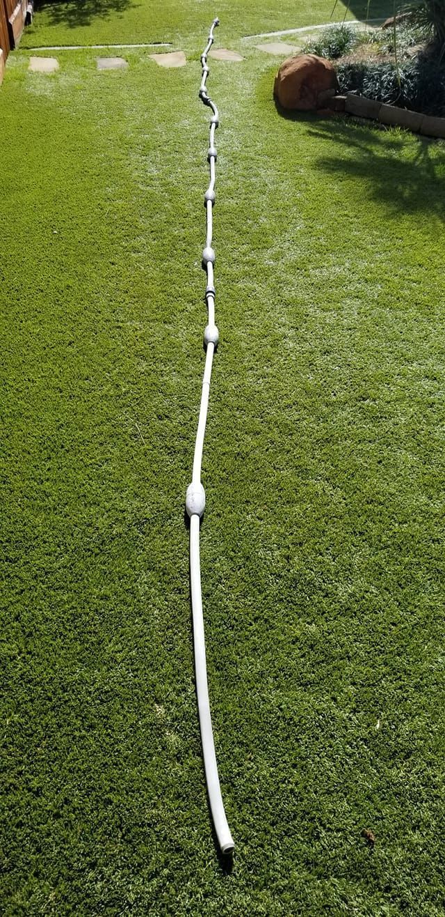 White hose laid across a grassy lawn under bright sunlight