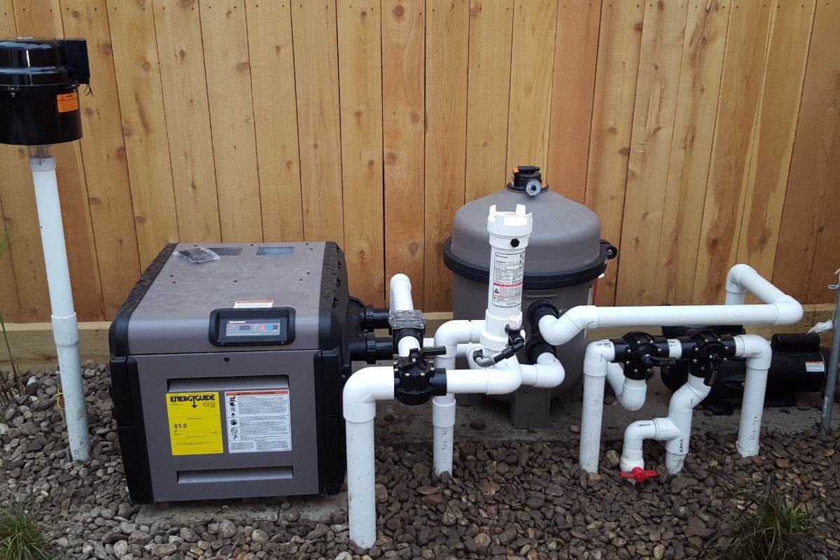 Pool heater and filter plumbing beside a wooden fence outdoors