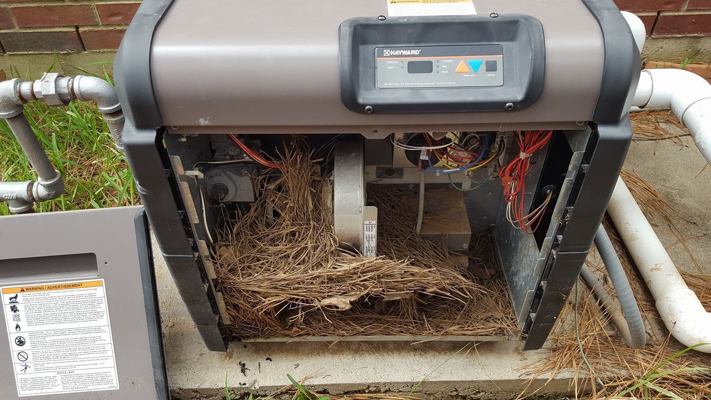 Open equipment cabinet with exposed wiring and debris beside outdoor pipes.