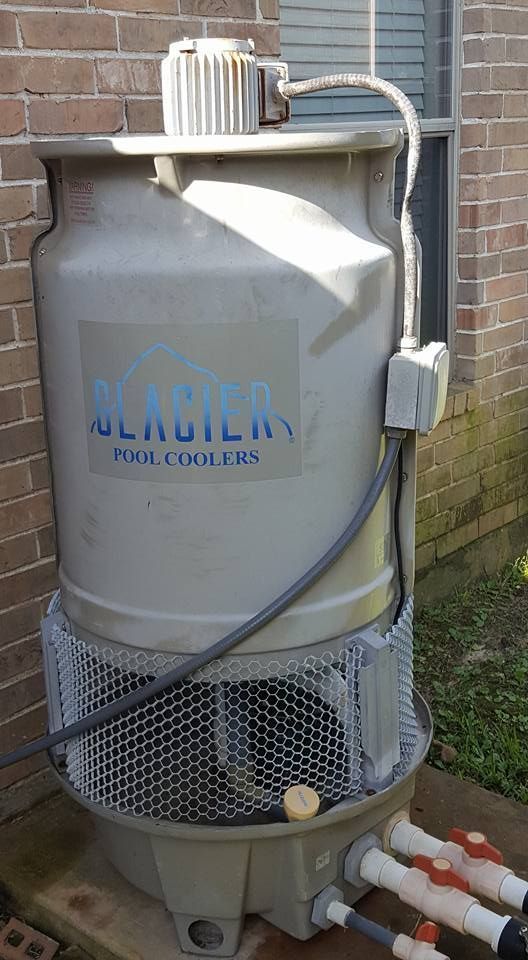 Large white industrial tank with pipes and hoses beside a brick wall outdoors