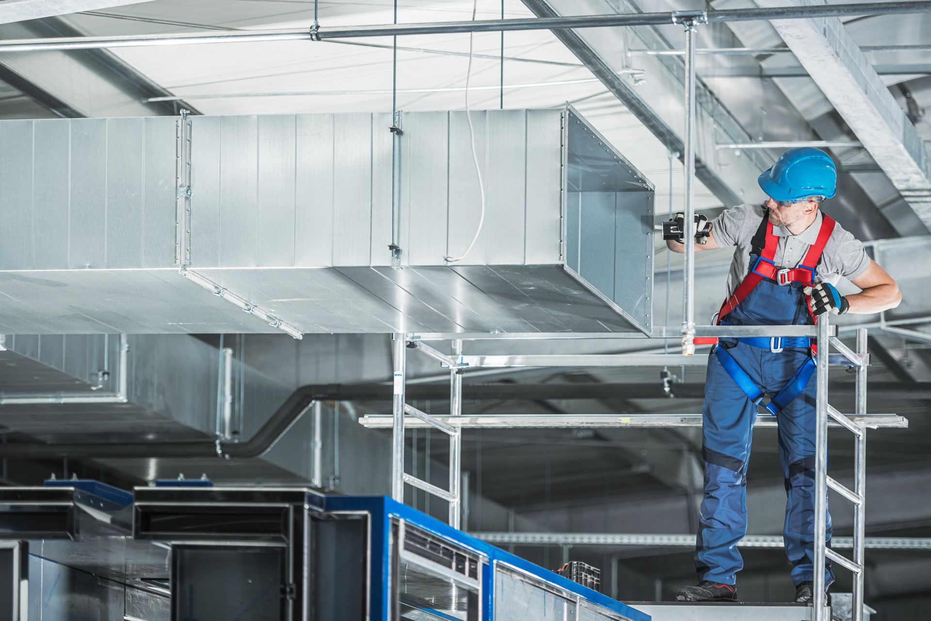 Technician in hard hat cleaning and servicing overhead air ducts from scaffolding. Technician in hard hat cleaning and servicing overhead air ducts from scaffolding.