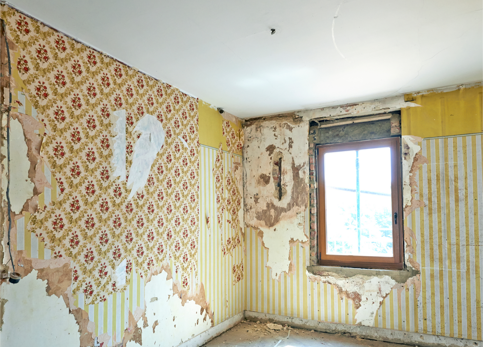 An empty room with peeling wallpaper and a window - Before Picture. 