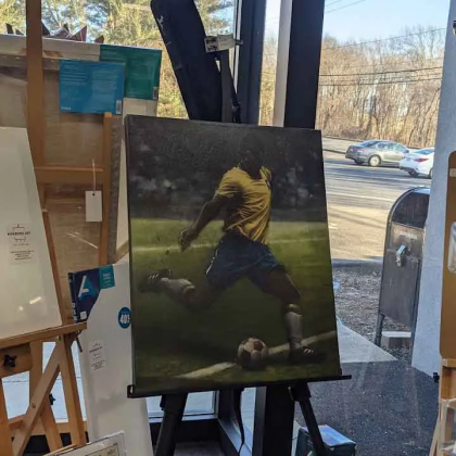 A painting of a man kicking a soccer ball on an easel