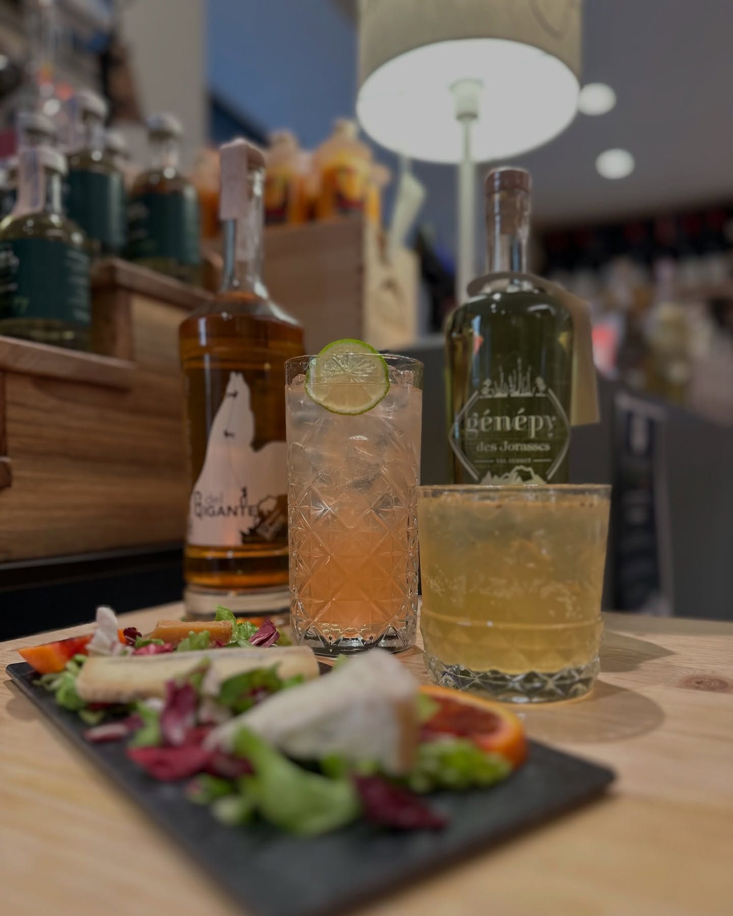 Cocktail su un bancone di legno con un colorato piatto di antipasti in primo piano.