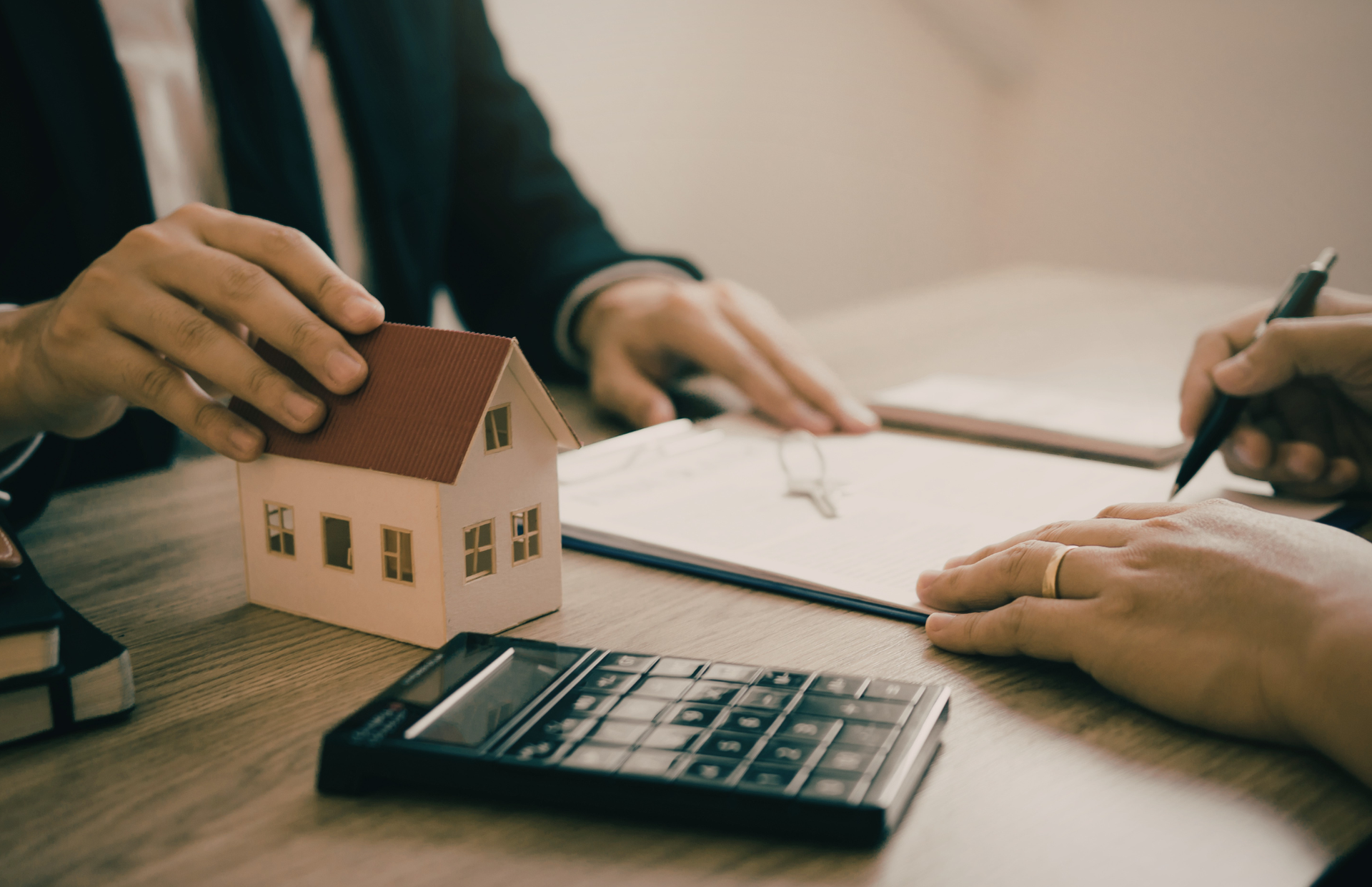 Hands and a small house model beside a calculator during a real estate meeting