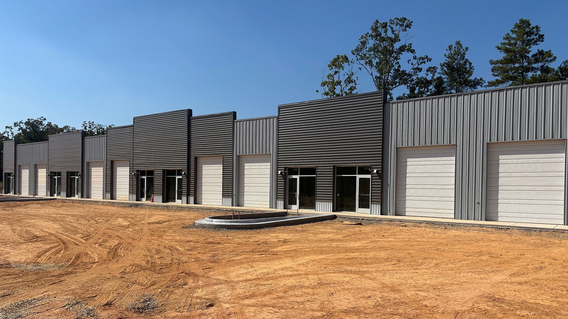 Row of modern commercial buildings under construction; corrugated metal facades, dirt lot.