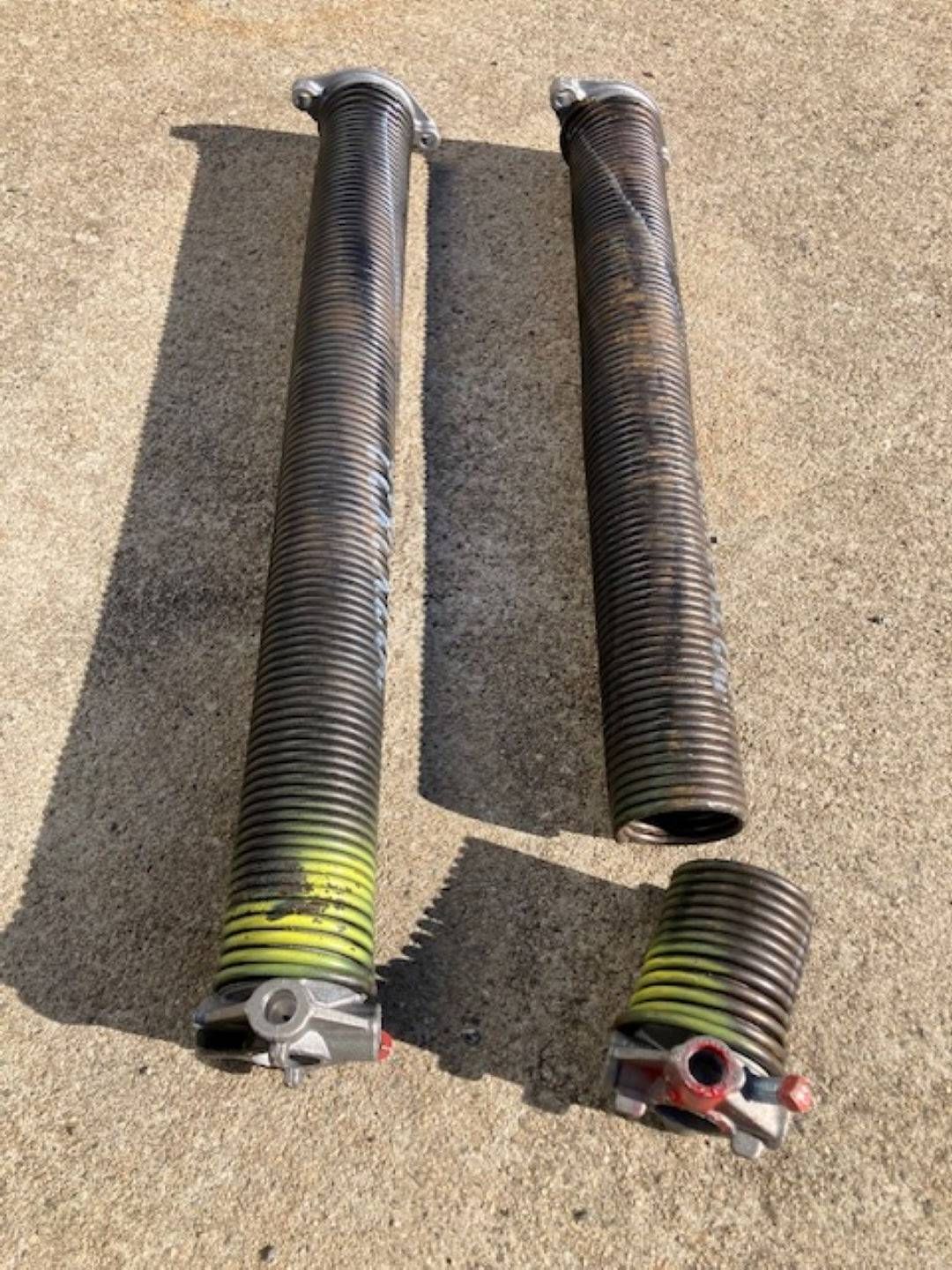 Two broken garage door springs on concrete. One spring is in two pieces, green and yellow paint on ends.